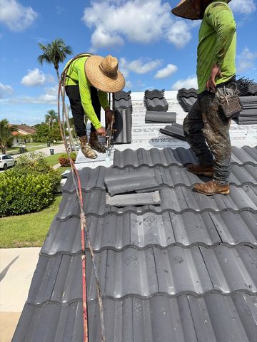 Workers repairing gray roof tiles on a sloped rooftop under a blue sky Workers repairing gray roof tiles on a sloped rooftop under a blue sky
