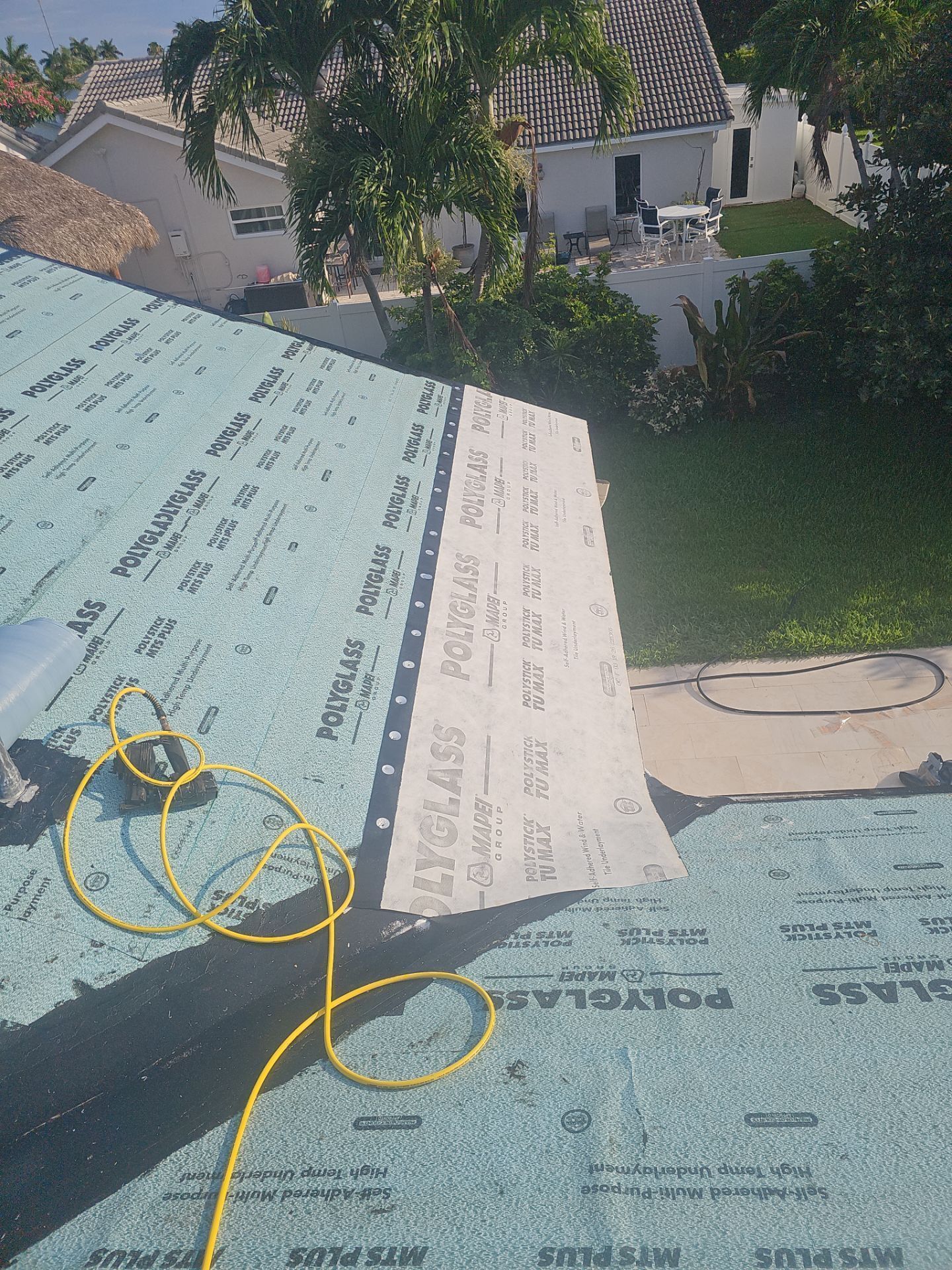 Roof under repair with green underlayment, yellow rope, and a house and trees in the background