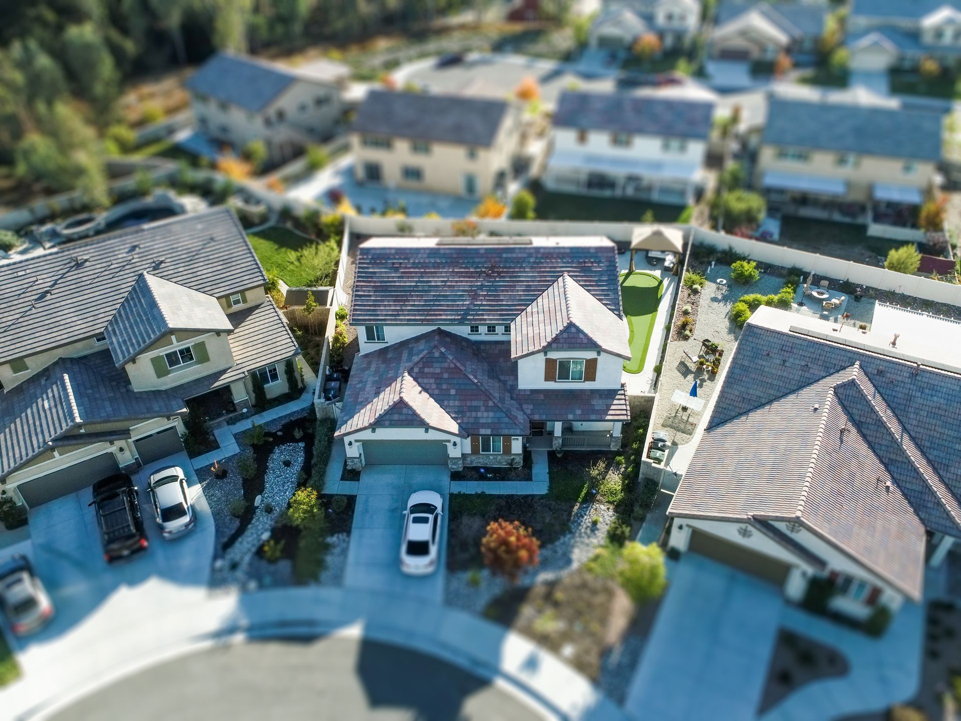 Aerial view of three suburban houses with driveways and parked cars on a curved street.