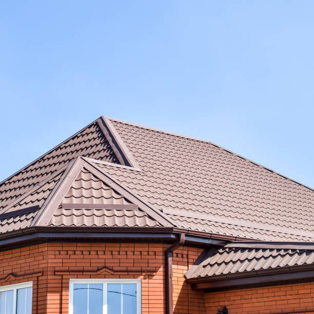 Close-up of a brick house roof with brown shingles and blue sky.