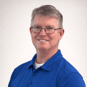 Portrait of a smiling person in glasses wearing a blue polo shirt against a light background