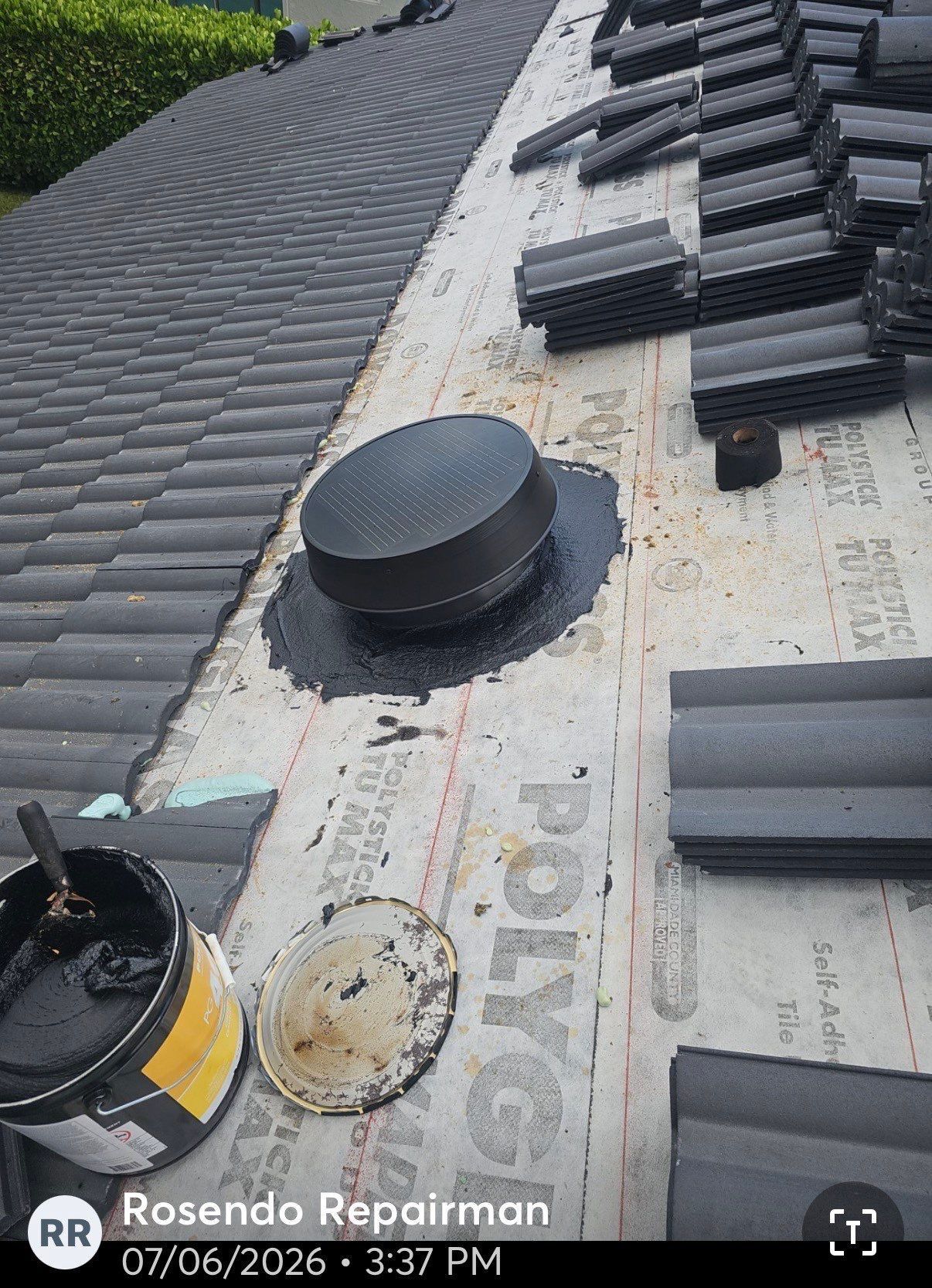Roof under construction with black tiles, vents, and stacked materials on waterproof underlayment.
