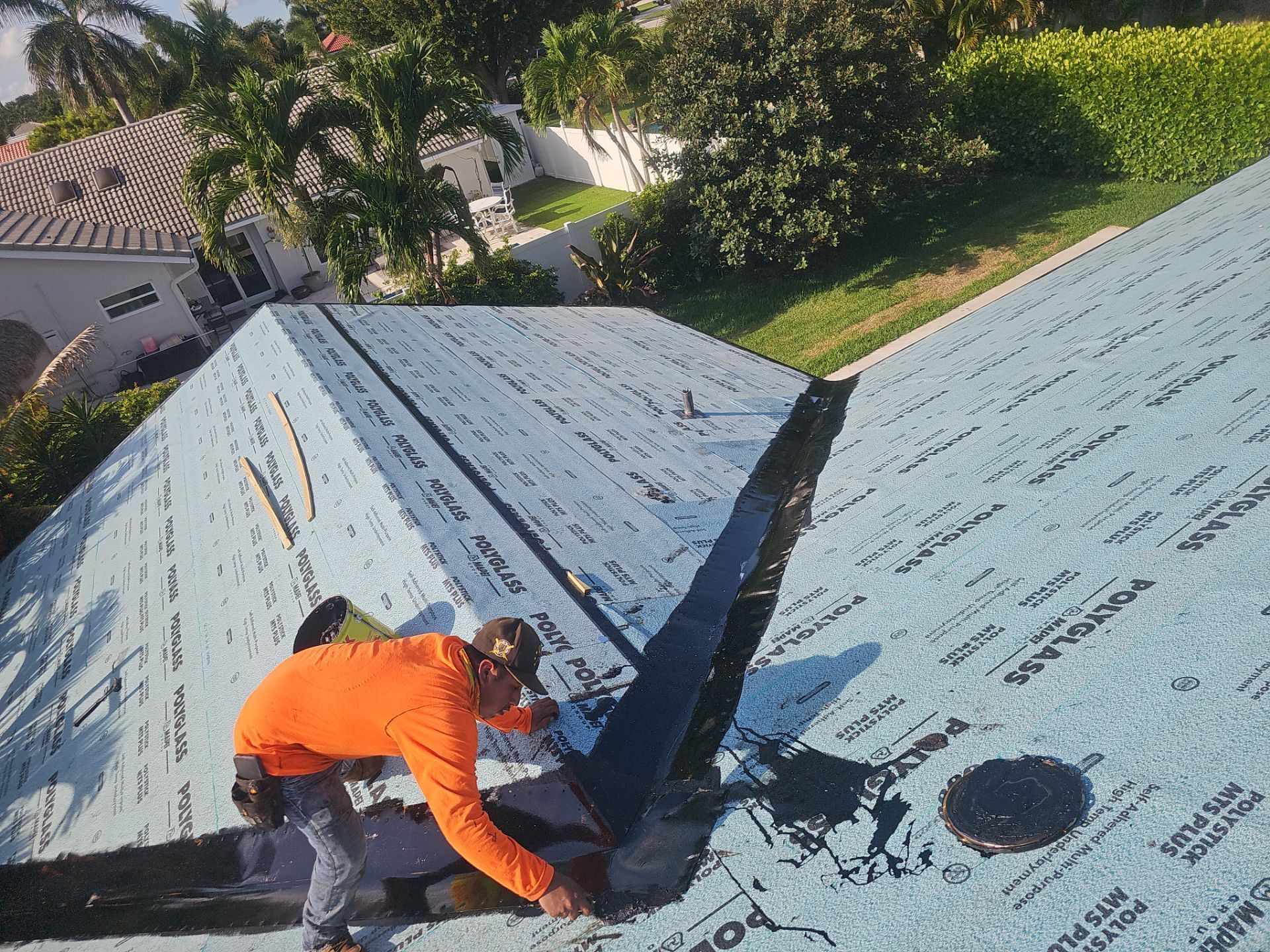 Worker in orange jacket repairs blue roof shingles on a house.