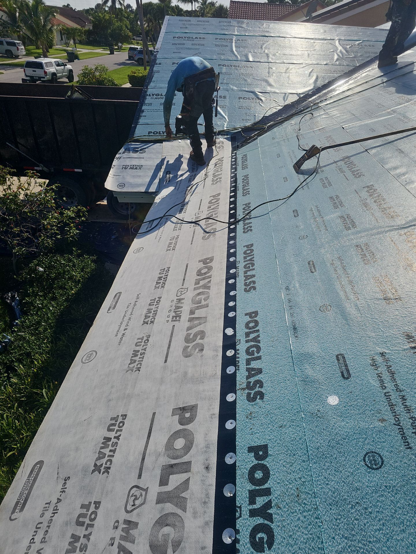 Worker installing blue roofing underlayment on a sloped roof in bright sunlight