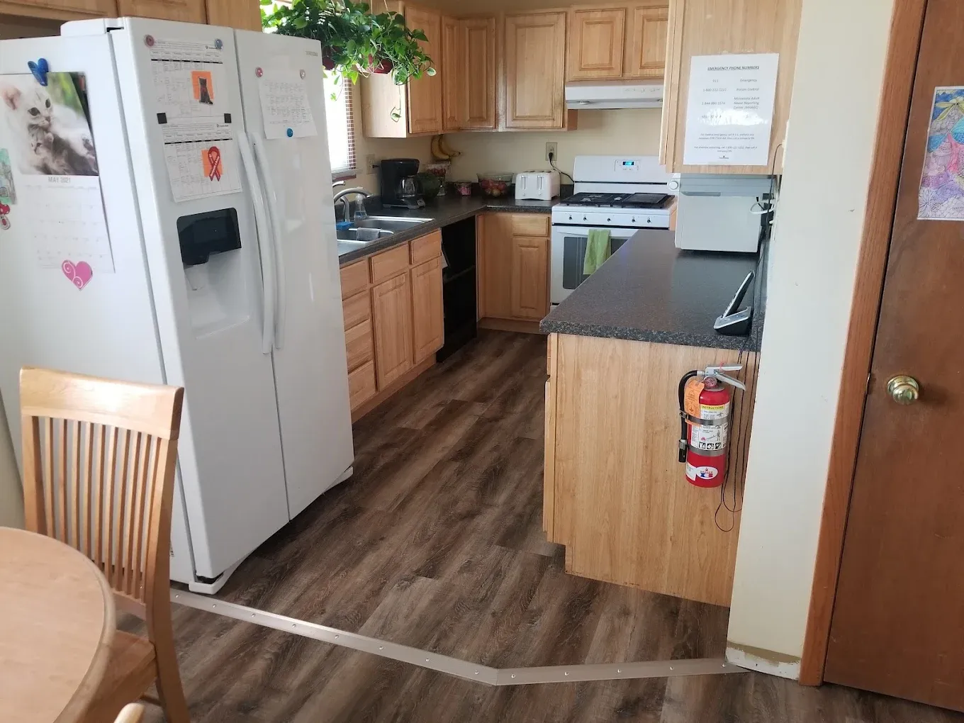 Kitchen with wood cabinets, appliances, and a fire extinguisher. Dark countertop, wood-look flooring.