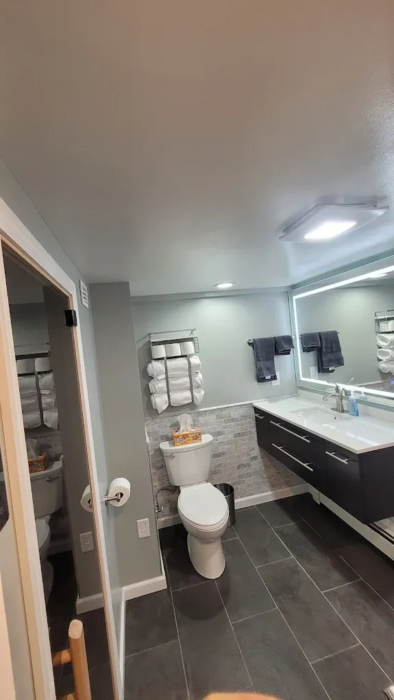 Bathroom with toilet, vanity, towels, and mirror. Gray walls and dark tile floor.