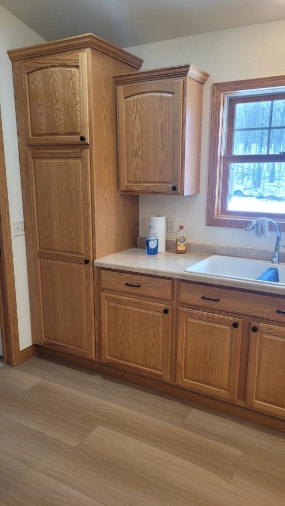 Oak kitchen cabinets next to a sink, window, and tan countertop.