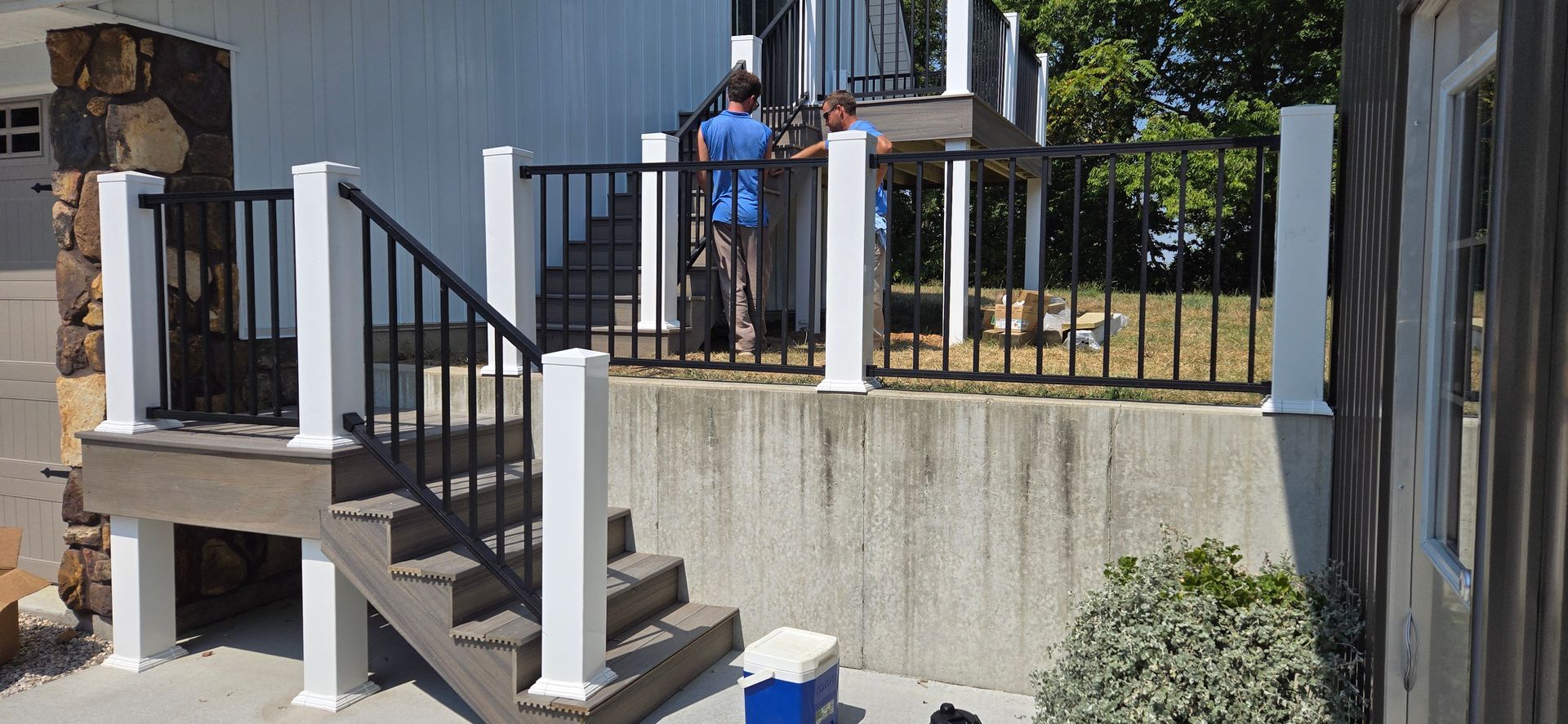Person in blue shirt standing on outdoor stair landing by a building and black railing