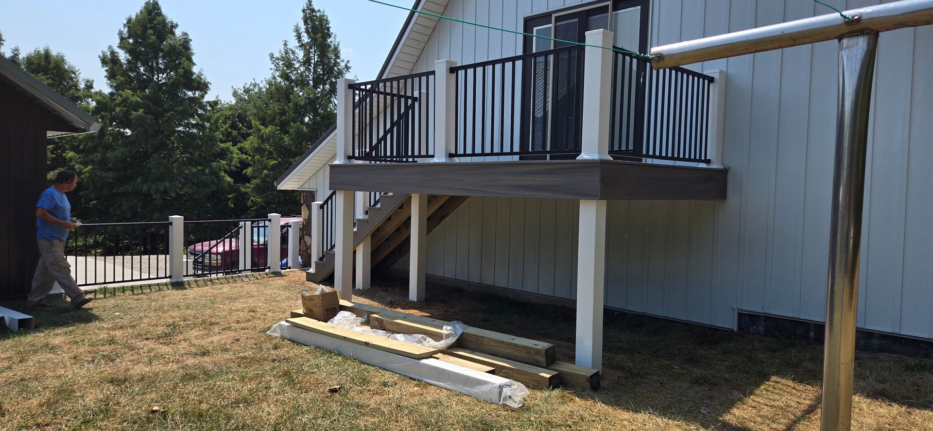 Small white house deck with stairs and black railings, viewed from the side on a sunny day