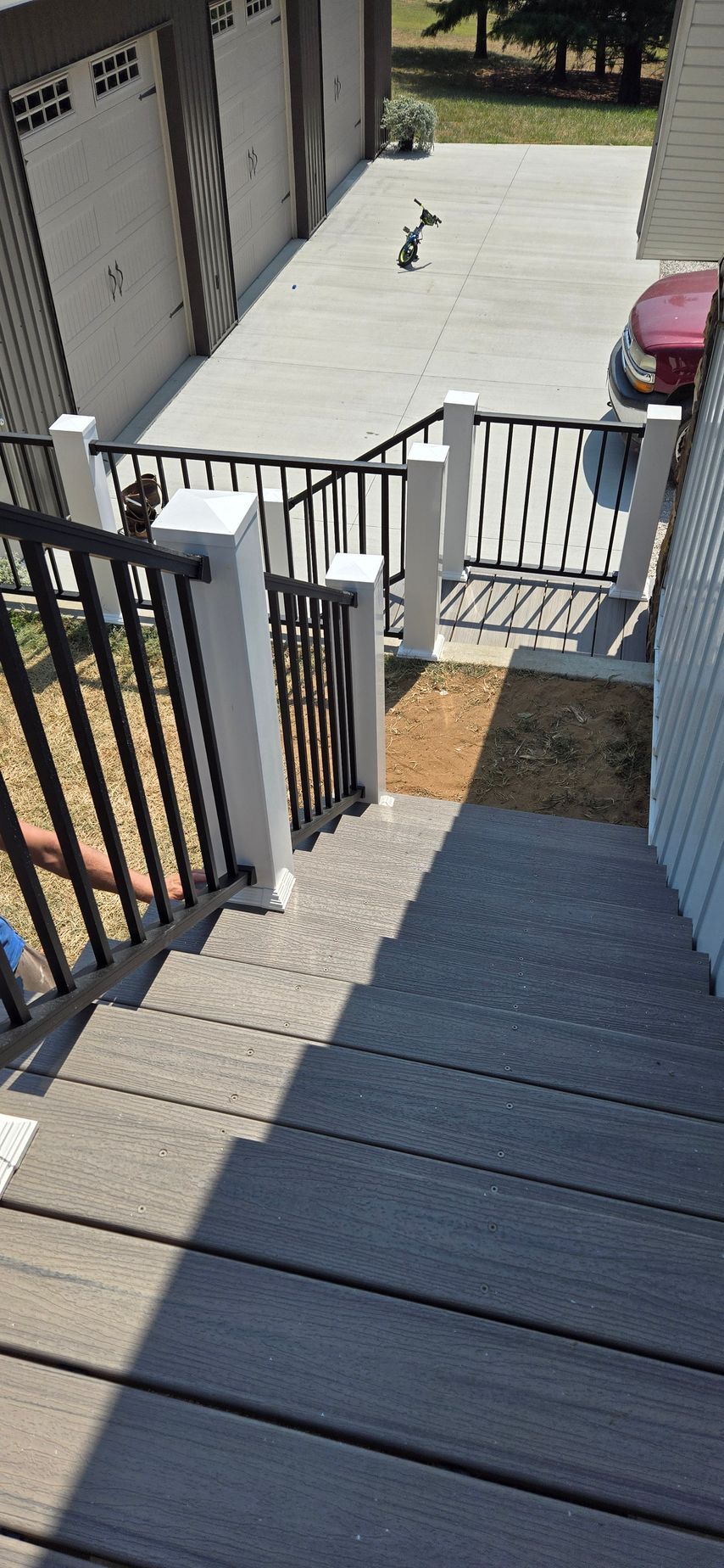 View from a stairway over a fenced landing to a concrete driveway, with a red car at right.