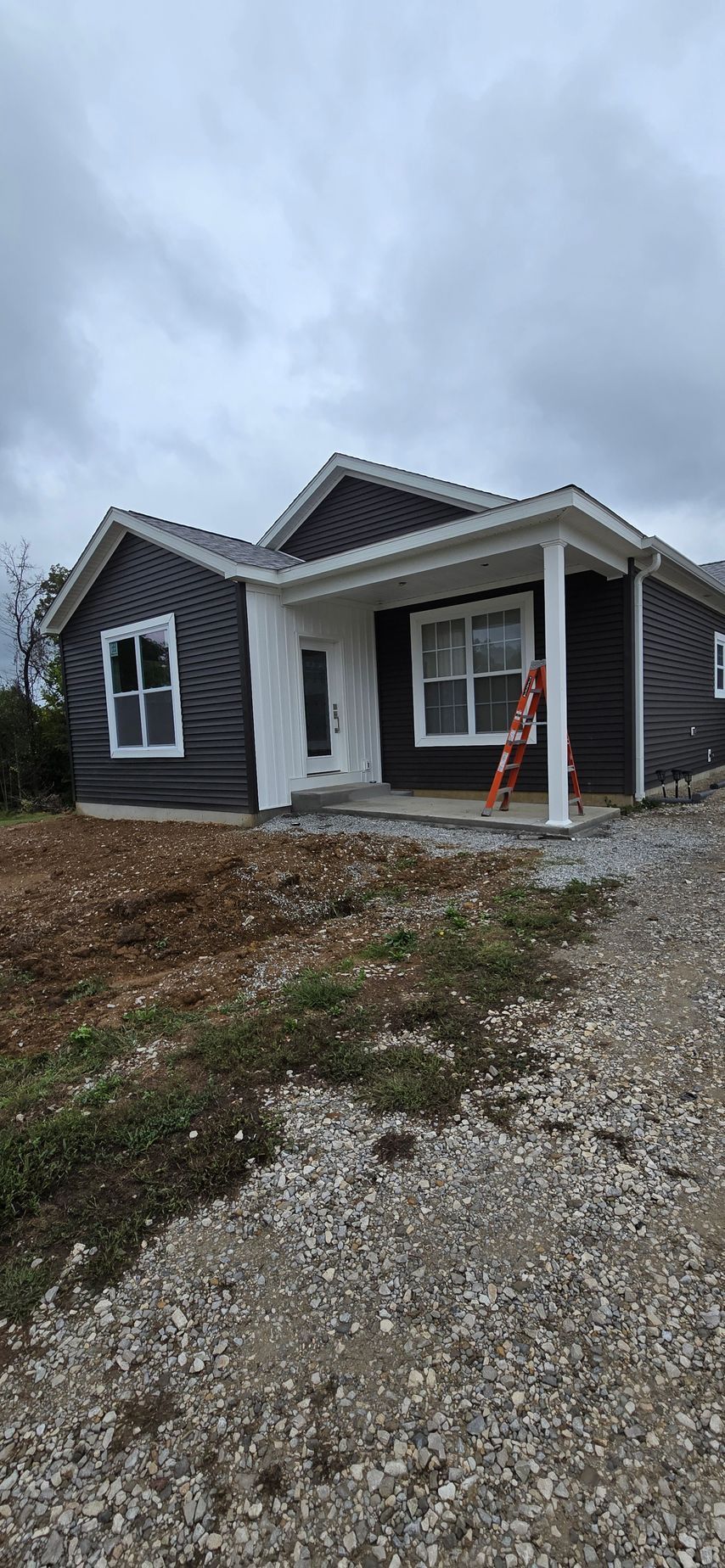 Gray single-story house with gravel driveway and orange traffic cone by the front porch