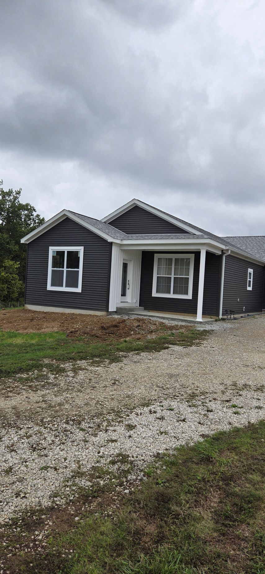 Small gray house with white trim and a gravel driveway under cloudy skies.