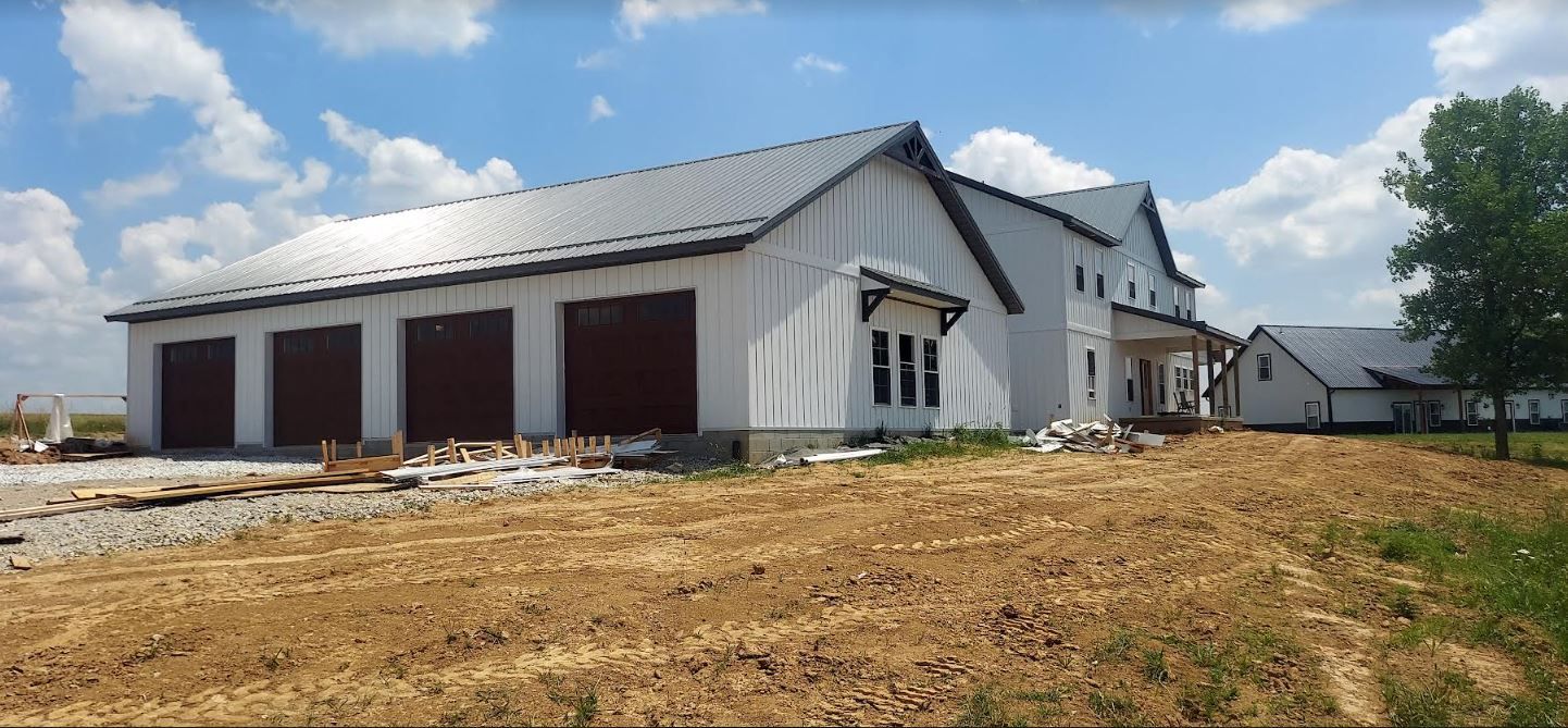 Large white building under construction on a dirt lot, with brown garage doors and blue sky.