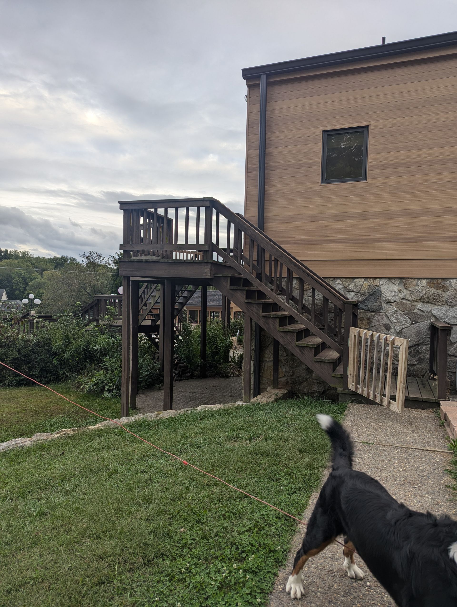 Wooden staircase and deck beside a brick building, with a black dog in the foreground.