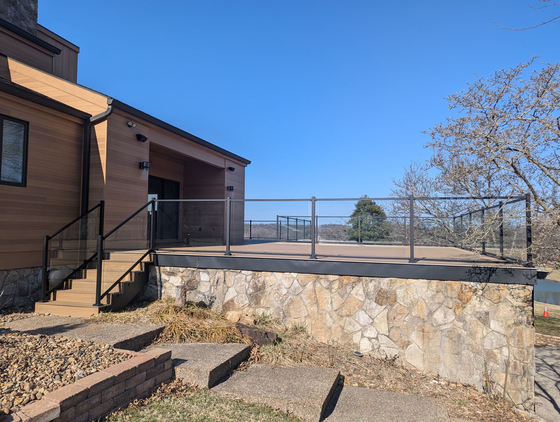 Brick building with steps leading to a stone terrace and fenced overlook under a clear blue sky