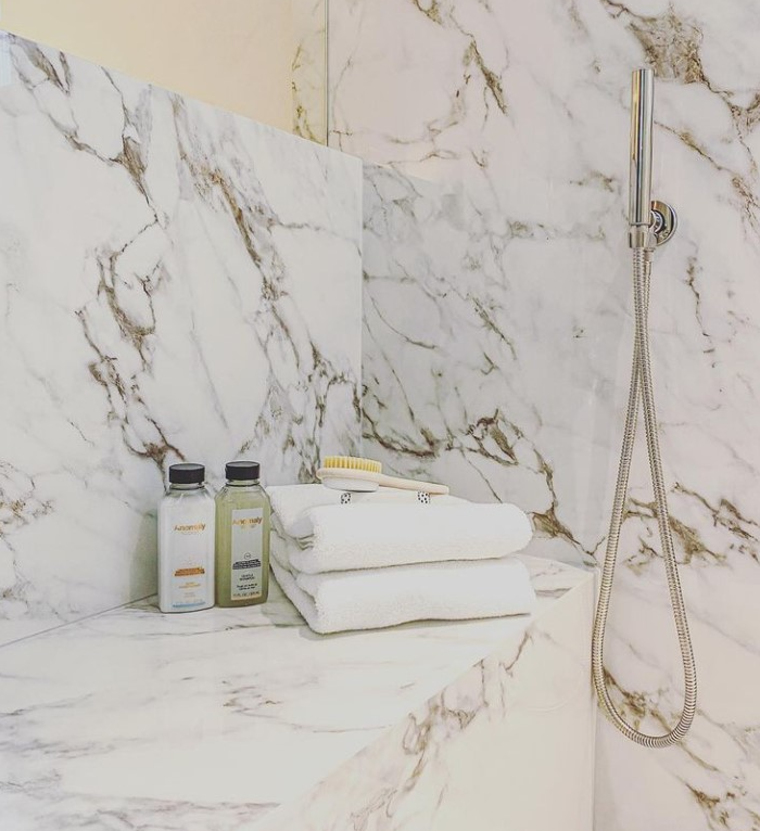 Marble shower nook with towels, toiletries, and a chrome handheld showerhead