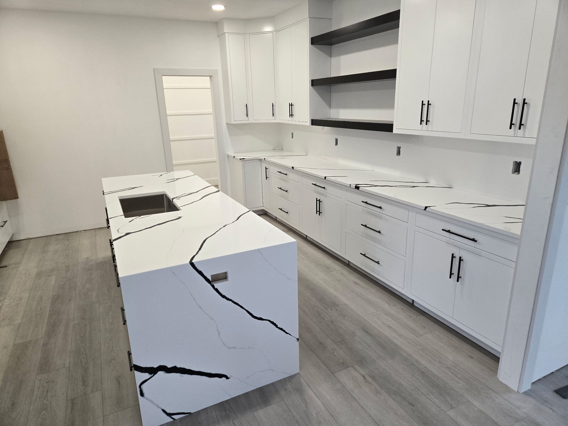Bright modern white kitchen with island, black countertop, and built-in cabinets and appliances