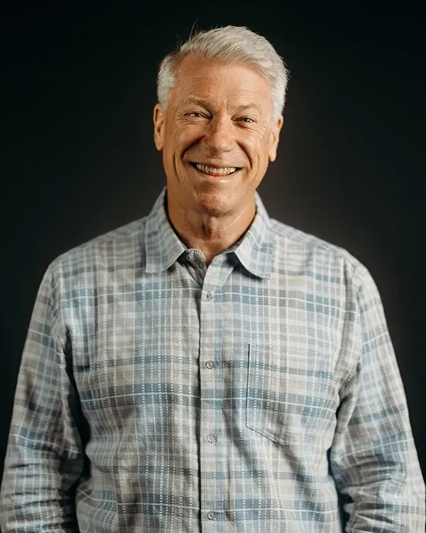 Man in plaid shirt smiling against a dark backdrop.