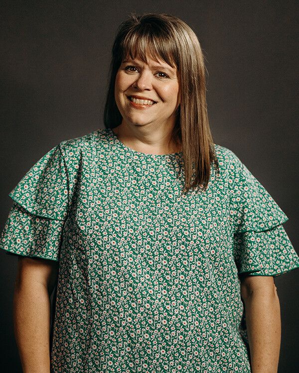 Woman with shoulder-length brown hair, smiling, wearing a green floral print top with ruffled sleeves.