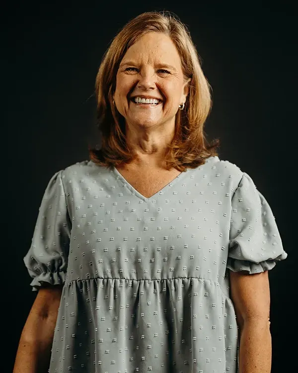 Woman smiling in a light blue dress, dark background.