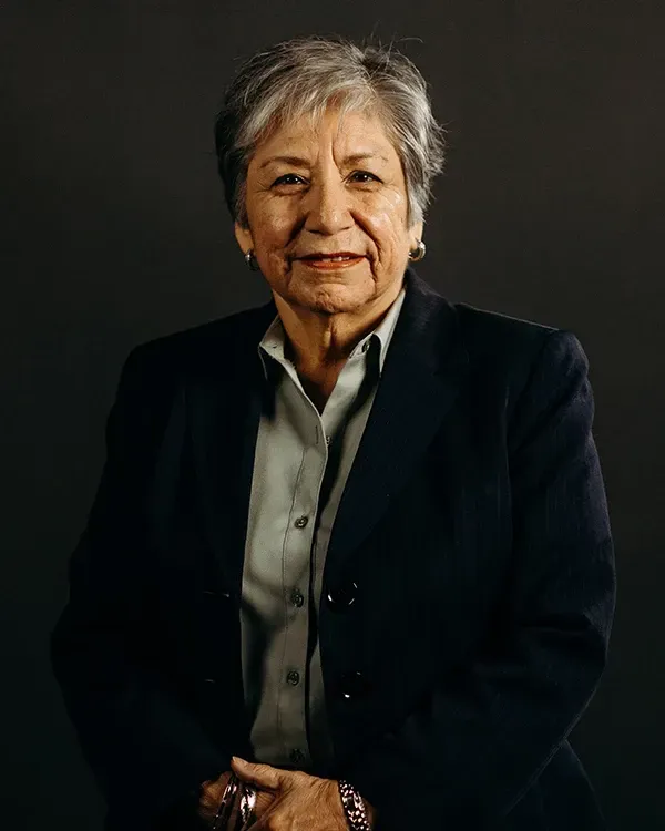 Woman in a blazer and button-up shirt poses in front of a dark background.