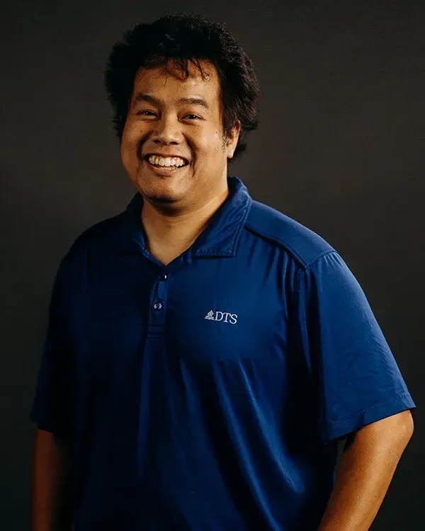 Smiling person in a blue polo shirt, against a dark gray background.