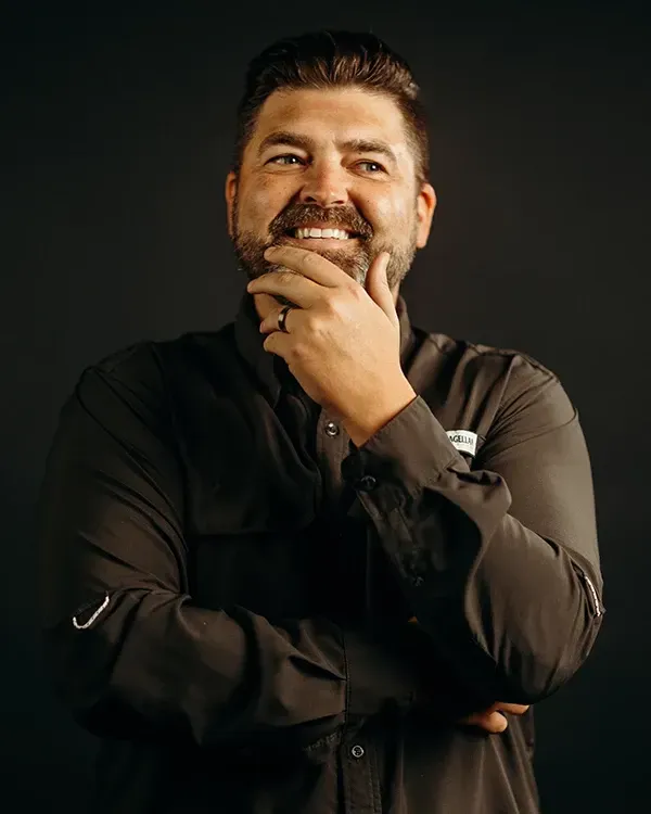 Man with beard, hand on chin, smiling, dark shirt, black background.