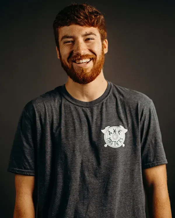 Man with reddish-brown hair and beard smiling broadly, wearing a gray t-shirt with a small graphic.