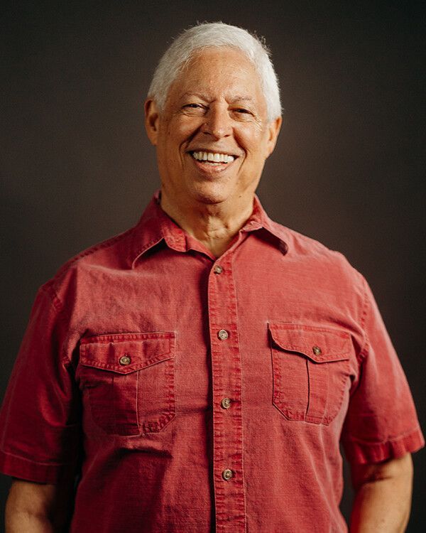 Smiling man in a red shirt, white hair, against a dark background.