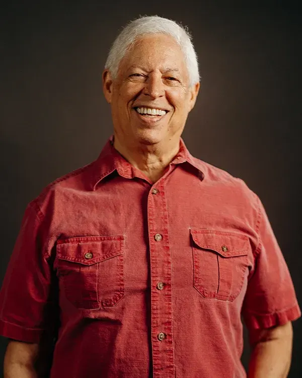 Smiling man in a red button-up shirt poses against a dark backdrop.