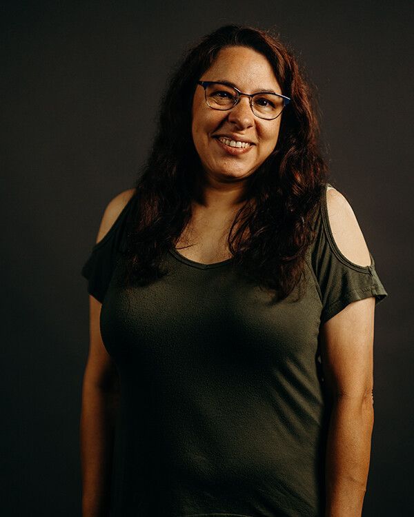 Woman with glasses smiles wearing a green shirt against a gray backdrop.