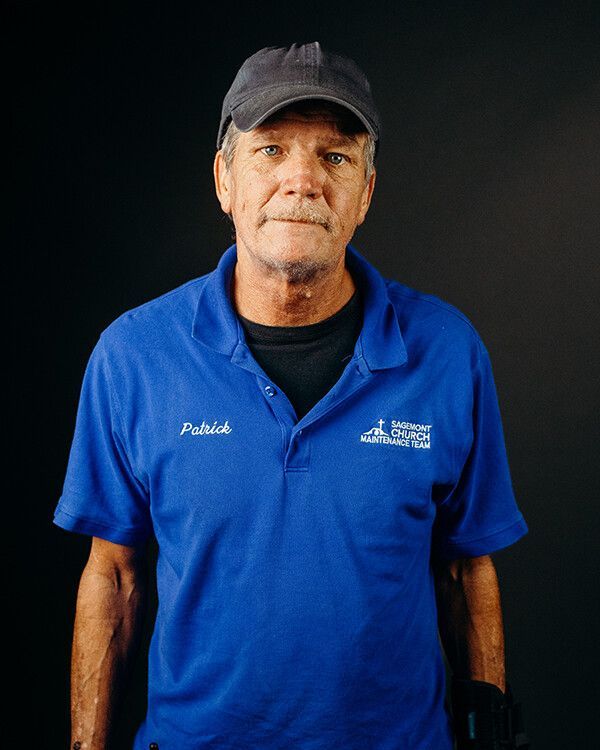 Man wearing blue polo and cap, standing in front of a black background.