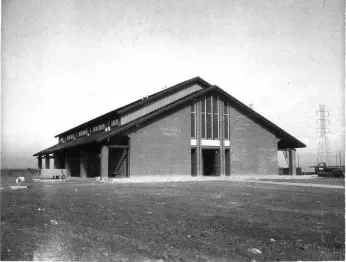 Brick building with a gabled roof and large glass windows. Construction site with power lines in the background.