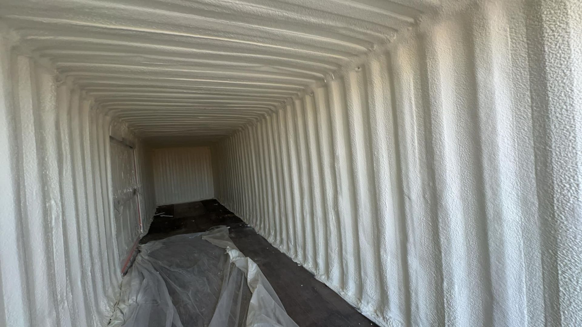 The inside of a shipping container is covered in white spray foam.