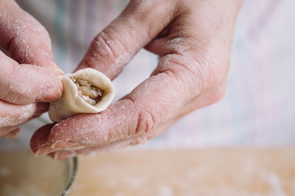 Mani che modellano un piccolo raviolo con le dita infarinate su una superficie di lavoro