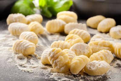Gnocchi freschi crudi, infarinati, su un piano di lavoro scuro con erbe aromatiche sullo sfondo.