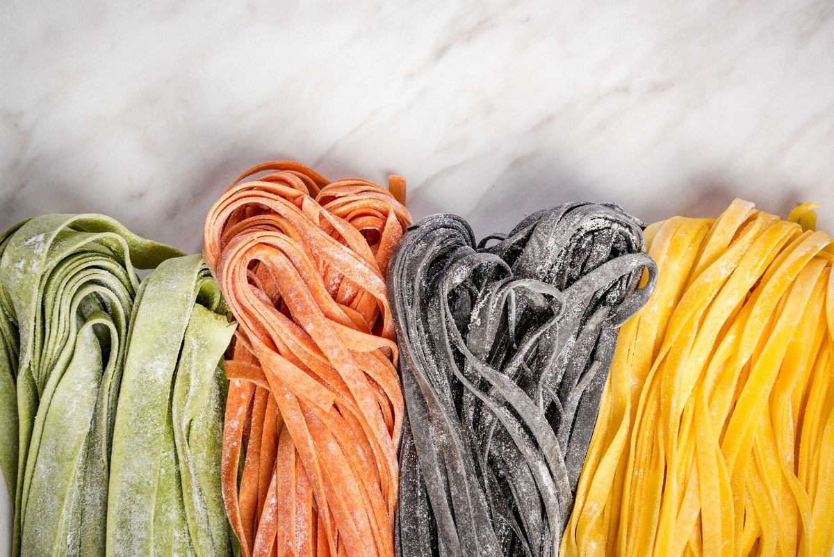 Quattro mazzi di pasta verdi, arancioni, neri e gialli su una superficie di marmo