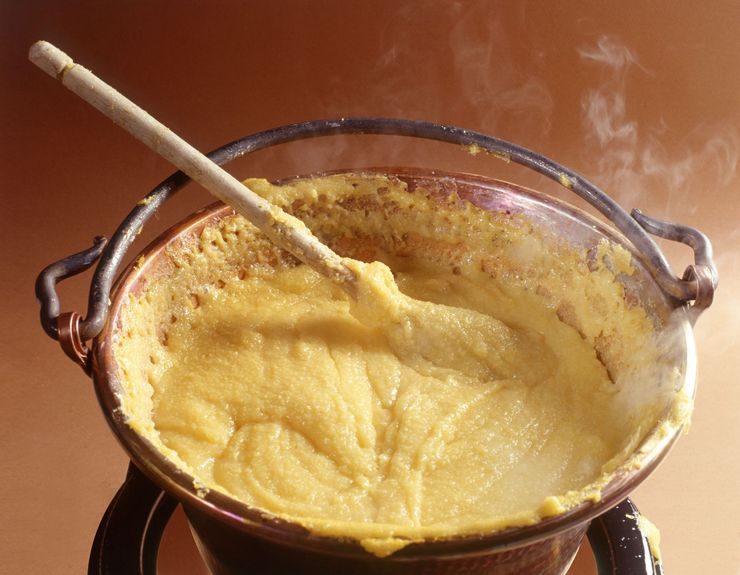 Una pentola di denso porridge giallo viene mescolata con un cucchiaio di legno, mentre si alza del vapore.