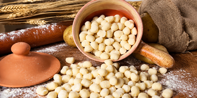 Assortimento di palline di pasta rotonde e grissini su una superficie rustica con ciotola e coperchio in terracotta.