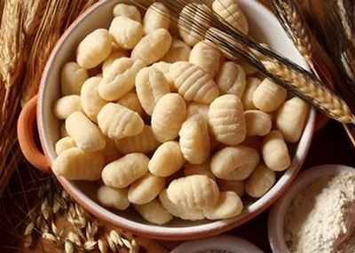 Ciotole di gnocchi crudi con forchetta di legno su una superficie rustica