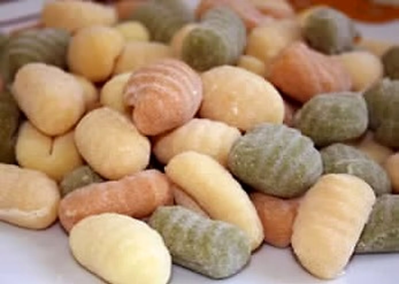 Su un piatto sono disposti vari pezzi di gnocchi colorati, tra cui varietà gialle, verdi e arancioni.