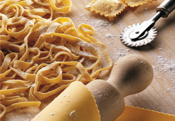 Pasta fresca, mattarello e tagliapasta su una superficie infarinata.
