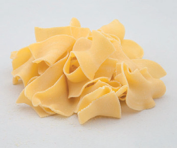 Pasta a farfalla di colore giallo pallido ammucchiata su uno sfondo bianco.