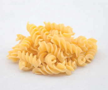 Pila di pasta fusilli cruda su sfondo bianco