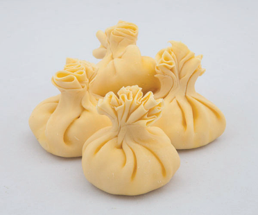 Quattro ravioli plissettati di colore giallo pallido su sfondo bianco.