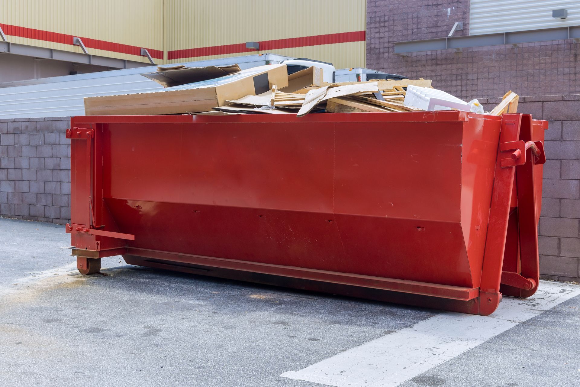 Red dumpster overflowing with wooden debris in an industrial yard