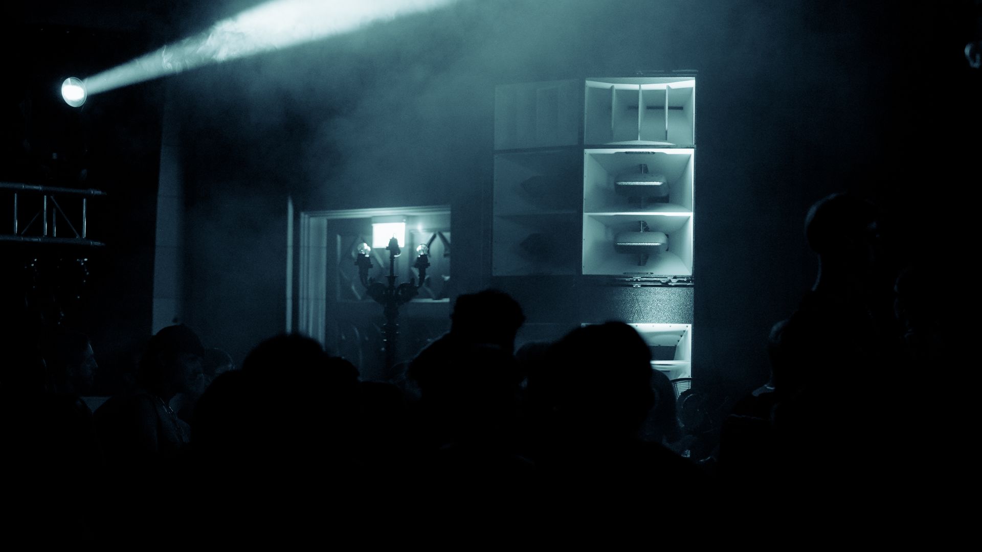 Dark club scene with a spotlight and silhouetted figures and a Lambda Labs QX3 loud speaker cluster.