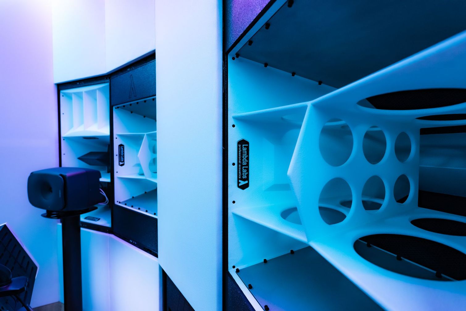 A complex, multi-chambered speaker system with white and black components, illuminated with blue light.