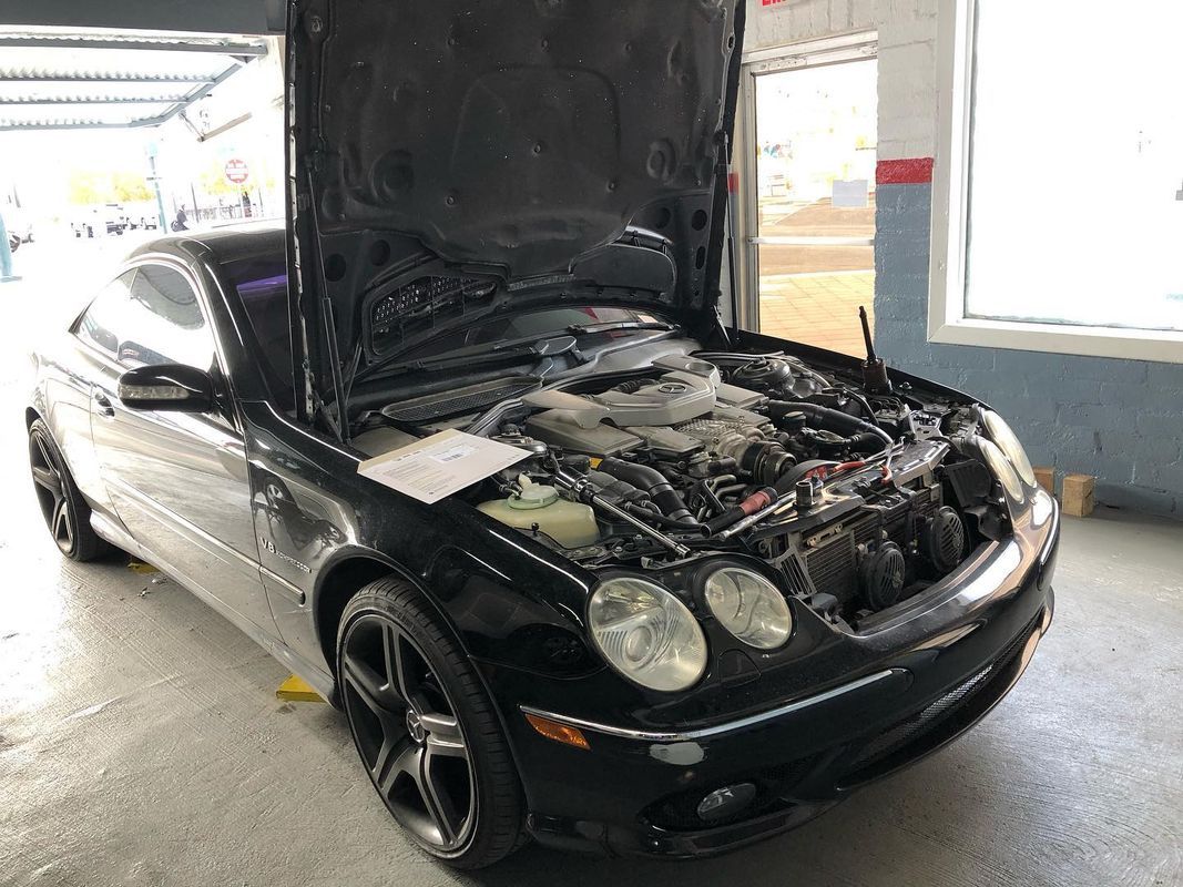 Black car with hood open in a garage, revealing engine components.