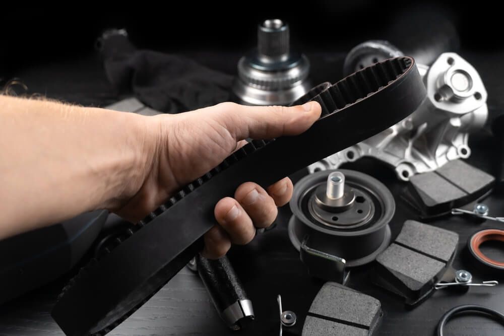 A person is holding a belt in their hand in front of a bunch of car parts.